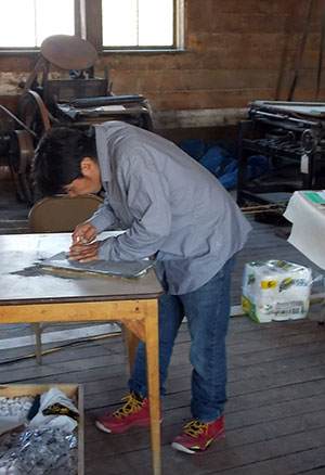 Nunavut artist Ashoona Ashoona carves a block to be used for stone-cut printmaking at the Dawson Daily News Print & Publishing Symposium.